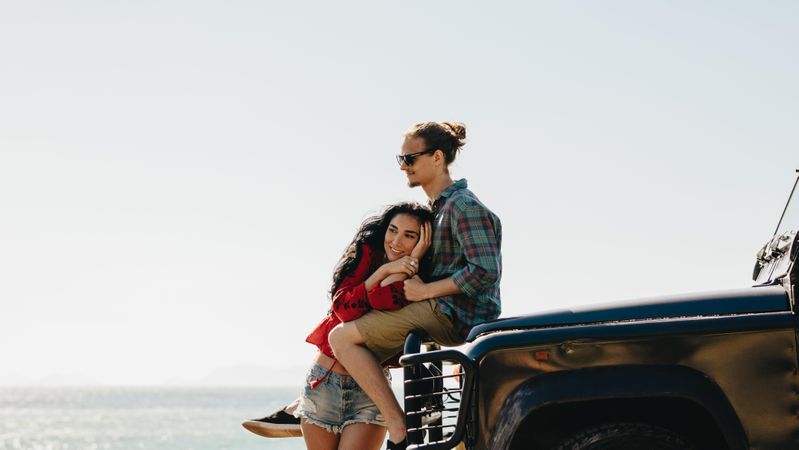 Young man and woman on road trip relaxing by their car at the beach
