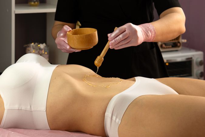 Beautician applies honey to abdomen with dipper during spa session.