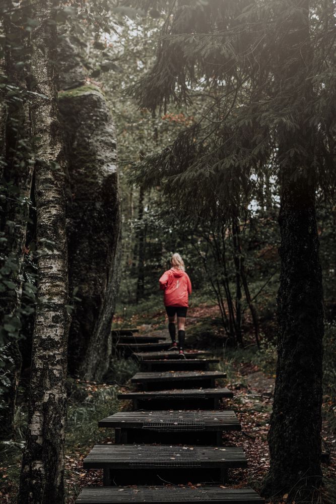 Woman in red jacket running on stairs between trees