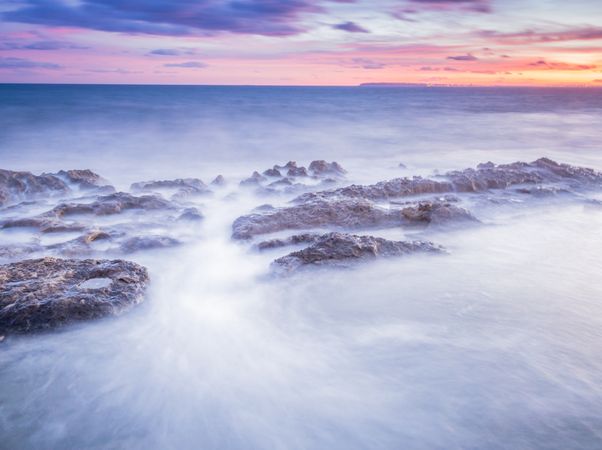 Sea waving near rough rocks during sunset