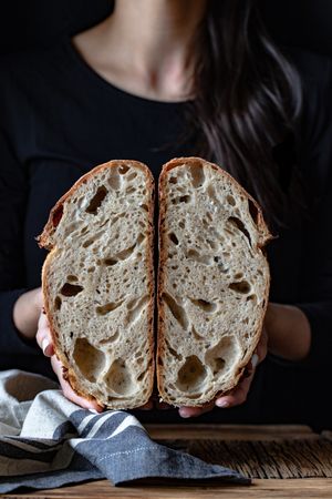 Crop person holding halved seeded bread