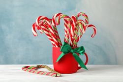 Candy canes in red cup on wooden background, space for text