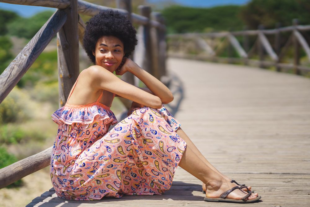 Smiling woman in maxi dress sitting on footbridge in the sun
