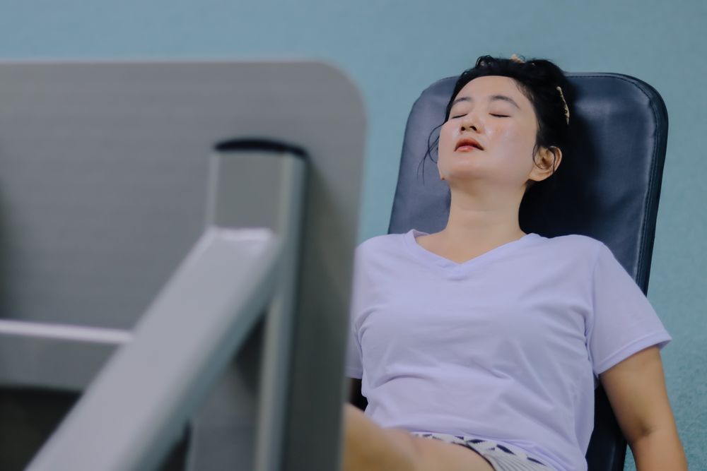 woman sitting on leg press machine, eyes closed, taking a break during workout session.