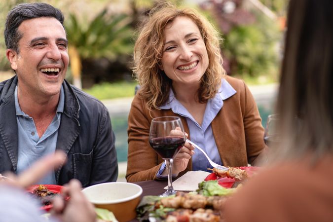 Two friends sharing a laugh and wine during a casual outdoor meal surrounded by nature and a spread of food