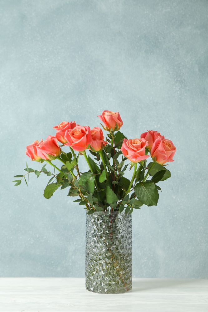 Vase with orange roses on table against light background