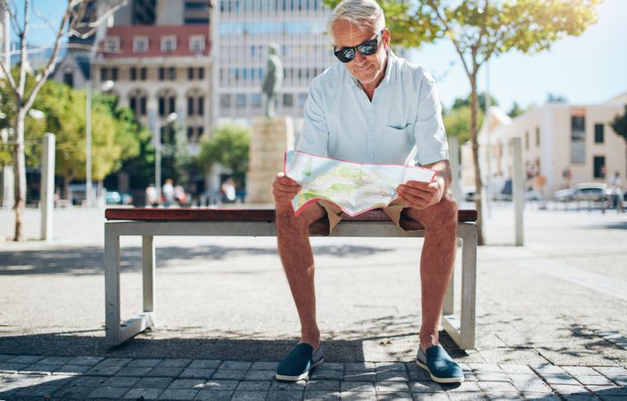 Male tourist sitting outdoors on a bench and reading a city map