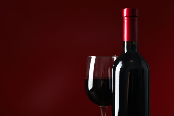 Bottle and glass with wine against red background, copy space