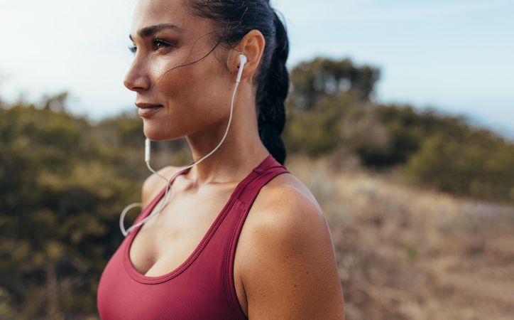 Side view of woman athlete with earphones standing outdoors before a run