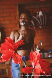 Woman in dark bra eating with spoon standing near red flowers in the kitchen beMLAb