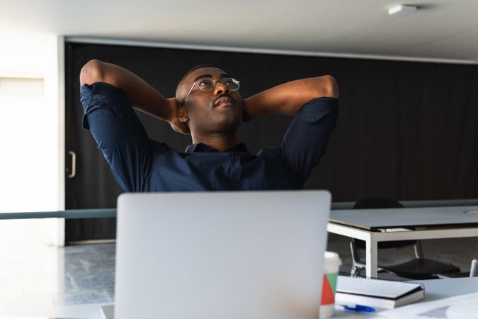 Black man taking break from work near laptop in office