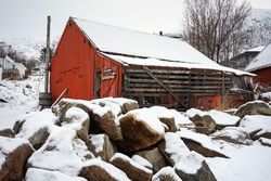 Large red barn against snowy hill and residential houses in countryside