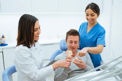 Smiling dentist and assistant showing structure of teeth on pros