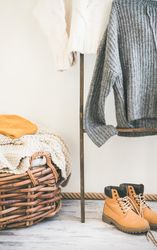 Woolen sweaters, grey scarf, winter boots on modern garment rack, with thatched basket, close up