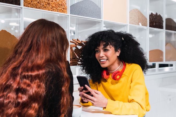 Positive multiethnic female friends using smartphones and laughing in cafe