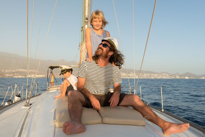 Man with smiling children and sitting on deck of yacht in sea
