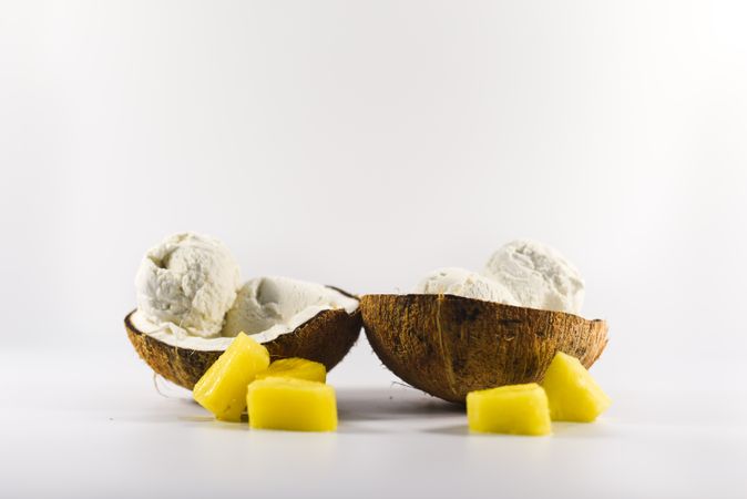 Side view of two coconut shells with ice cream and pineapple fruit chunks