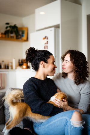 Happy female couple smiling at each other on sofa