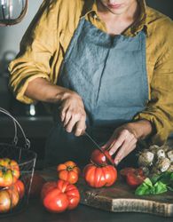 Woman in yellow chopping large tomatoes on wooden board