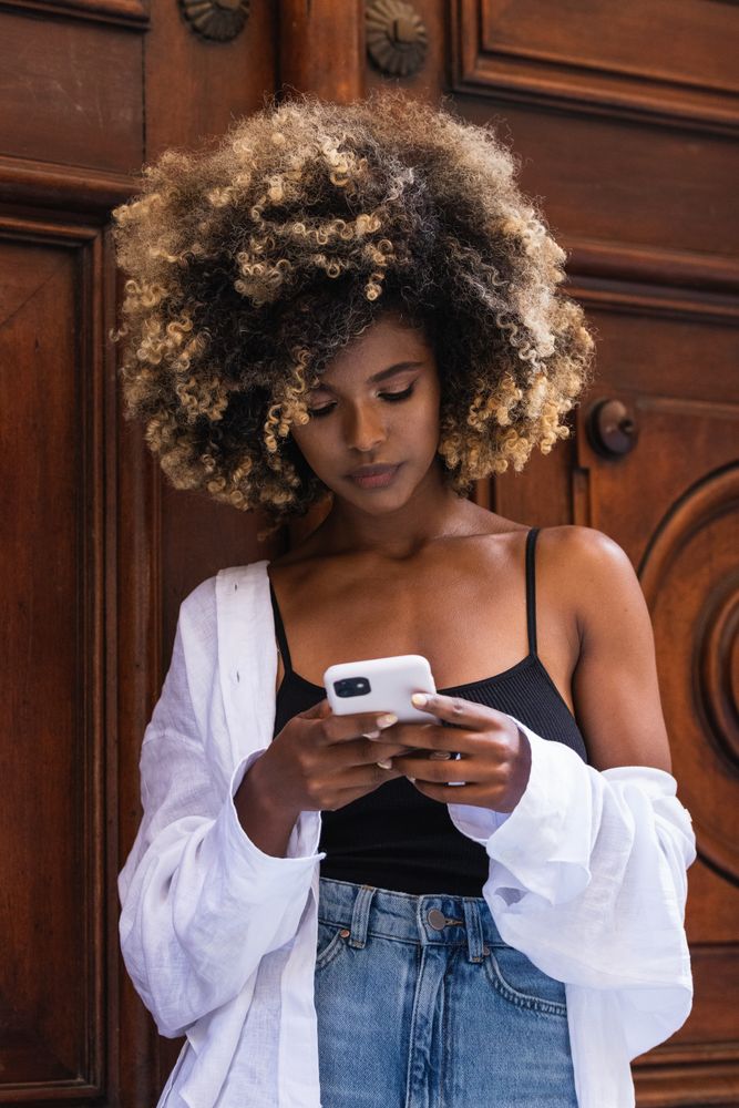 Black woman browsing smartphone near old gates old wooden door
