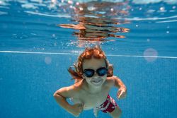 Excited boy in goggles swimming in pool