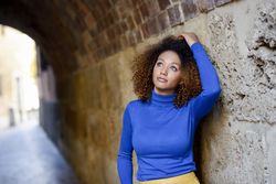 Nonchalant woman with curly hair looking up and touching her hair standing in European street
