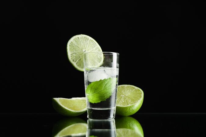 Tequila shot with lime, mint and ice against dark background