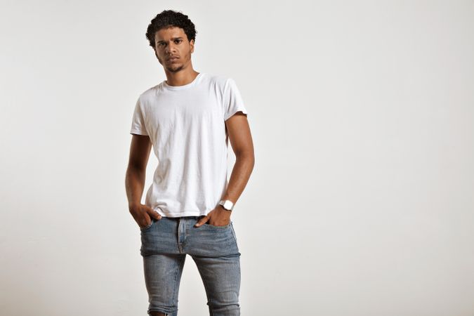 Man with neutral expression in plain t-shirt and jeans with hands in pocket in studio shoot