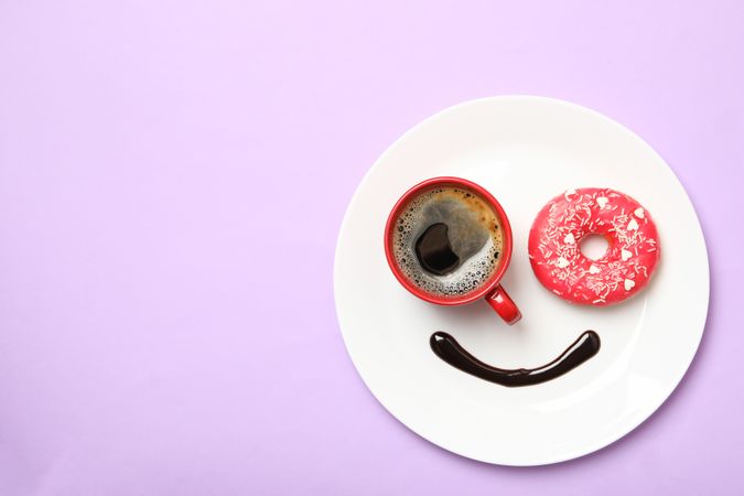 Smile face made of plate with donut, chocolate sauce and coffee on violet background