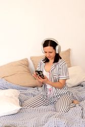 Woman reacting to smartphone content with headphones in bed.