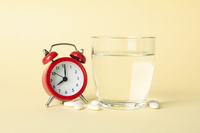 Glass of water with pills next to alarm clock in beige room