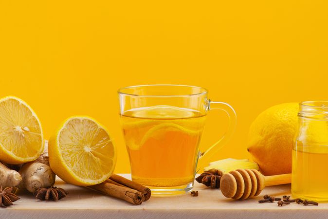 Cup of tea with lemon slices, surrounded by lemon halves, cinnamon and ginger