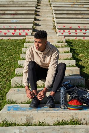 Serious Latino man tying shoelaces before training on skateboard