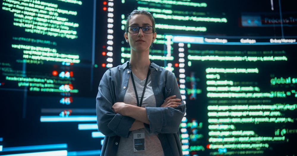 Portrait of Woman Looking at Camera and Crossing Arms With Big Digital Screens Glitching in the Background.