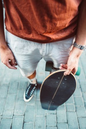 Sportive man carrying longboard while standing on street