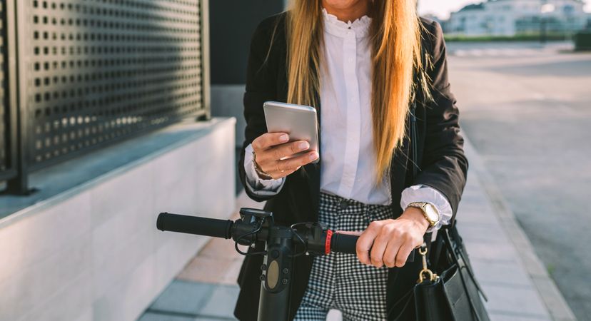 Unrecognizable businesswoman with e-scooter looking at cellphone