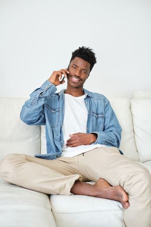 Content Black man talking on smartphone on sofa in house
