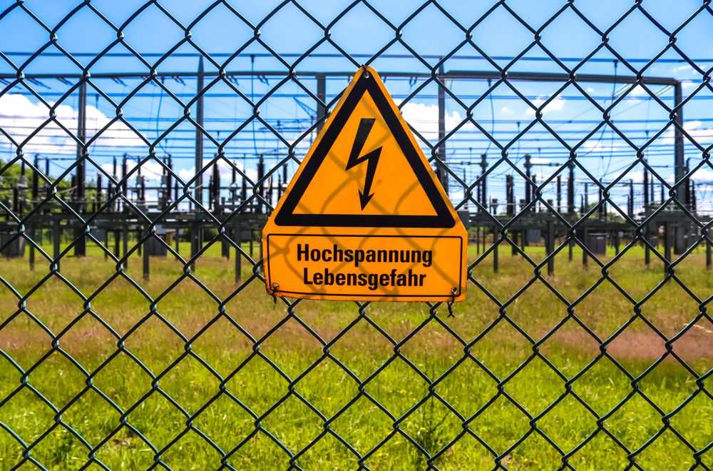 Sign showing the words high voltage in german language at the fence of a big substation distributing electric energy with lots power lines on a sunny day