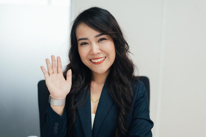 Asian woman in business causal waving at camera