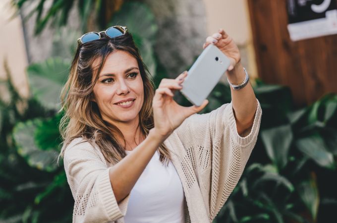 Smiling woman taking selfie in street city full of plants