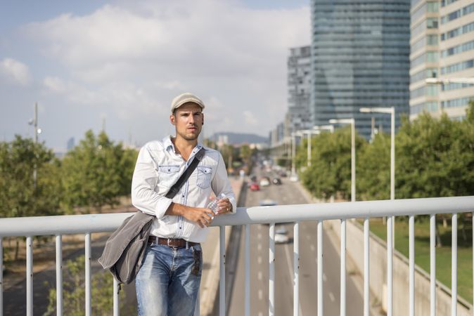 Male in denim with city traffic below standing on bridge