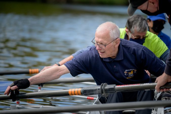 Grey haired man reaching for oar in water