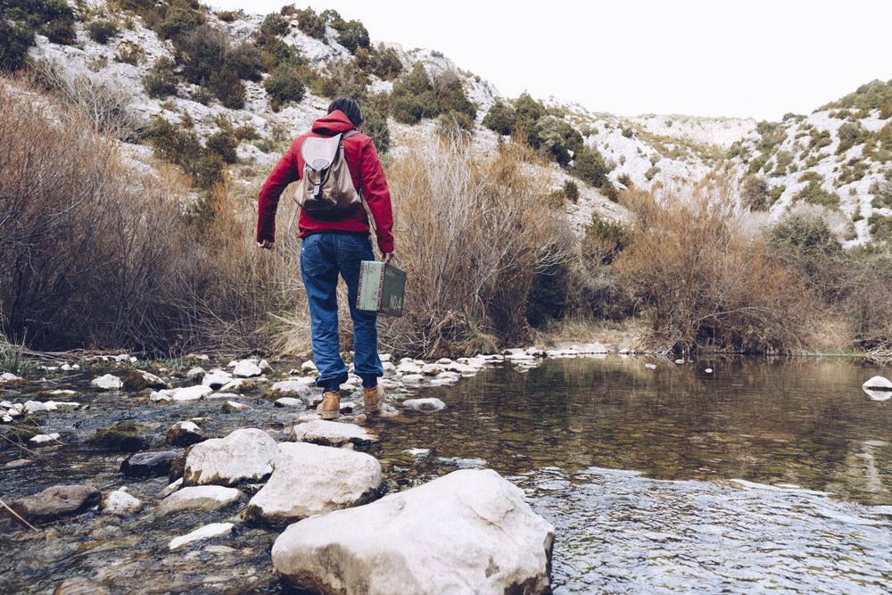Woman with case jumping on rocks above stream