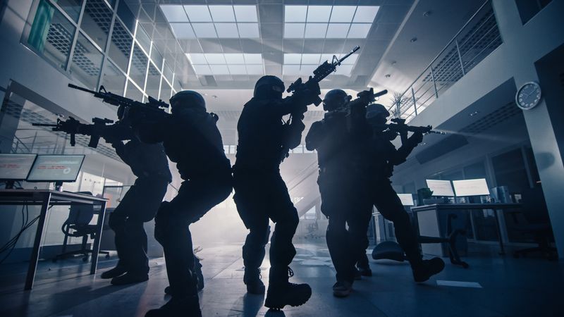 Masked Team of Armed SWAT Police Officers Move in a Hall of a Dark Seized Office Building with Desks and Computers.