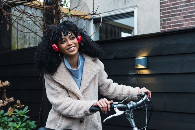 Cheerful Black woman in headphones with bicycle