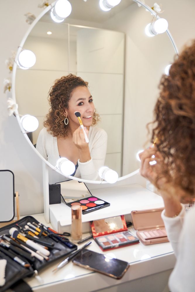 Smiling young female applying makeup on cheeks with brush