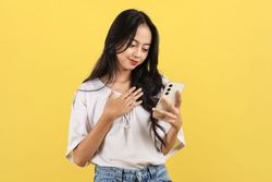 Portrait of Smiling Young Asian Woman in White Shirt Holding Mobile Phone with Hand on Chest