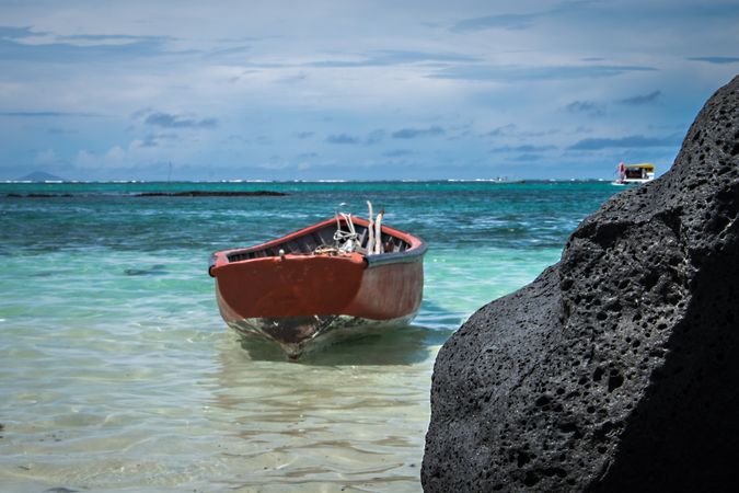 Small red boat in shallow tropical waters near dark rock