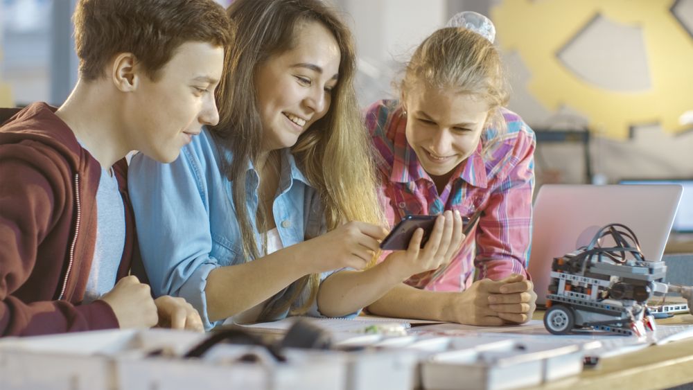 Boy and Two Girls Working on a Schools Science Class Project Watch Popular Videos on Smartphone.