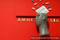 Model of bust with pills on red background and the words “Amnesia” copy space 0g1aA4